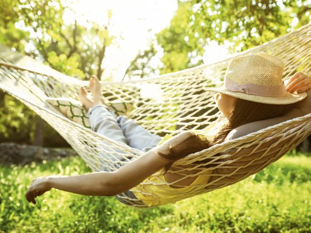 Young woman with hat resting in comfortable hammock at green garden